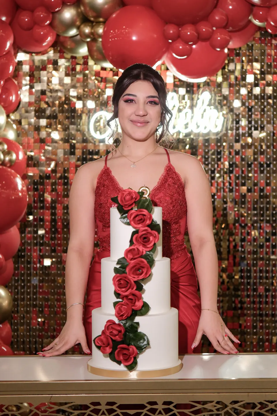 Festeggiata in abito rosso accanto alla torta con rose